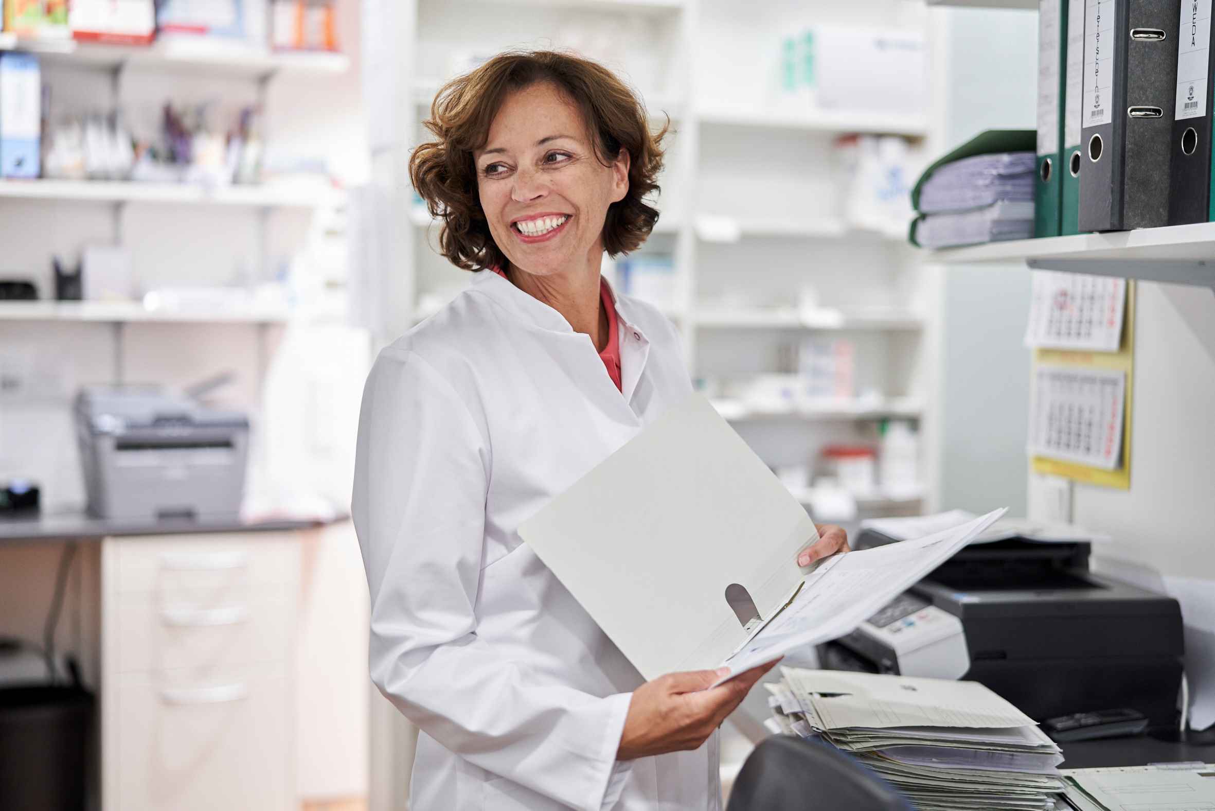 A pharmacist wears a white coat and smiles.